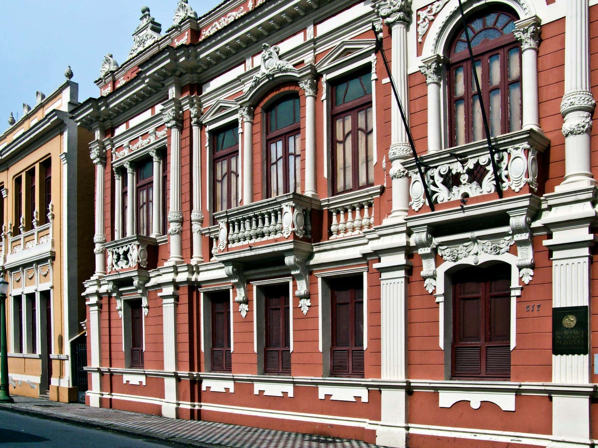 Fachada eclética em vermelho e branco de um edifício histórico brasileiro, com janelas altas e ornamentos