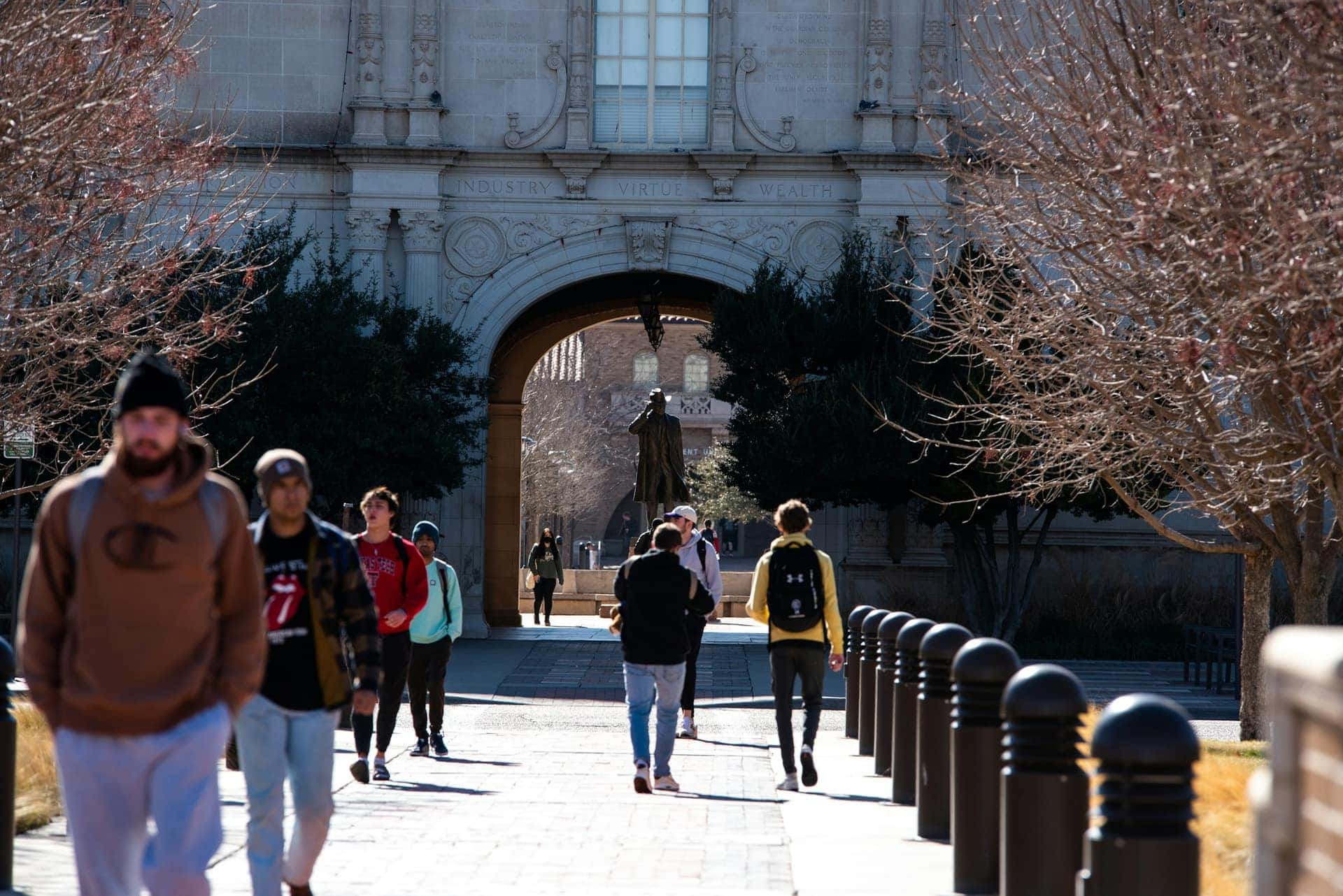 Estudantes atravessam um arco de pedra de um edifício universitário histórico sob a luz suave da tarde