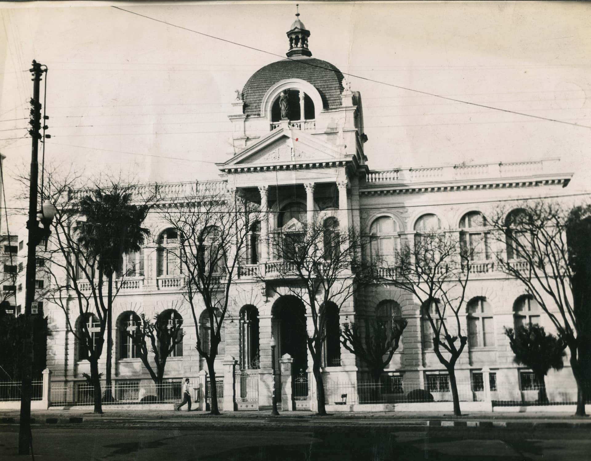 Fotografia antiga em preto e branco de um palacete eclético com cúpula e jardim fronteiro numa cidade brasileira