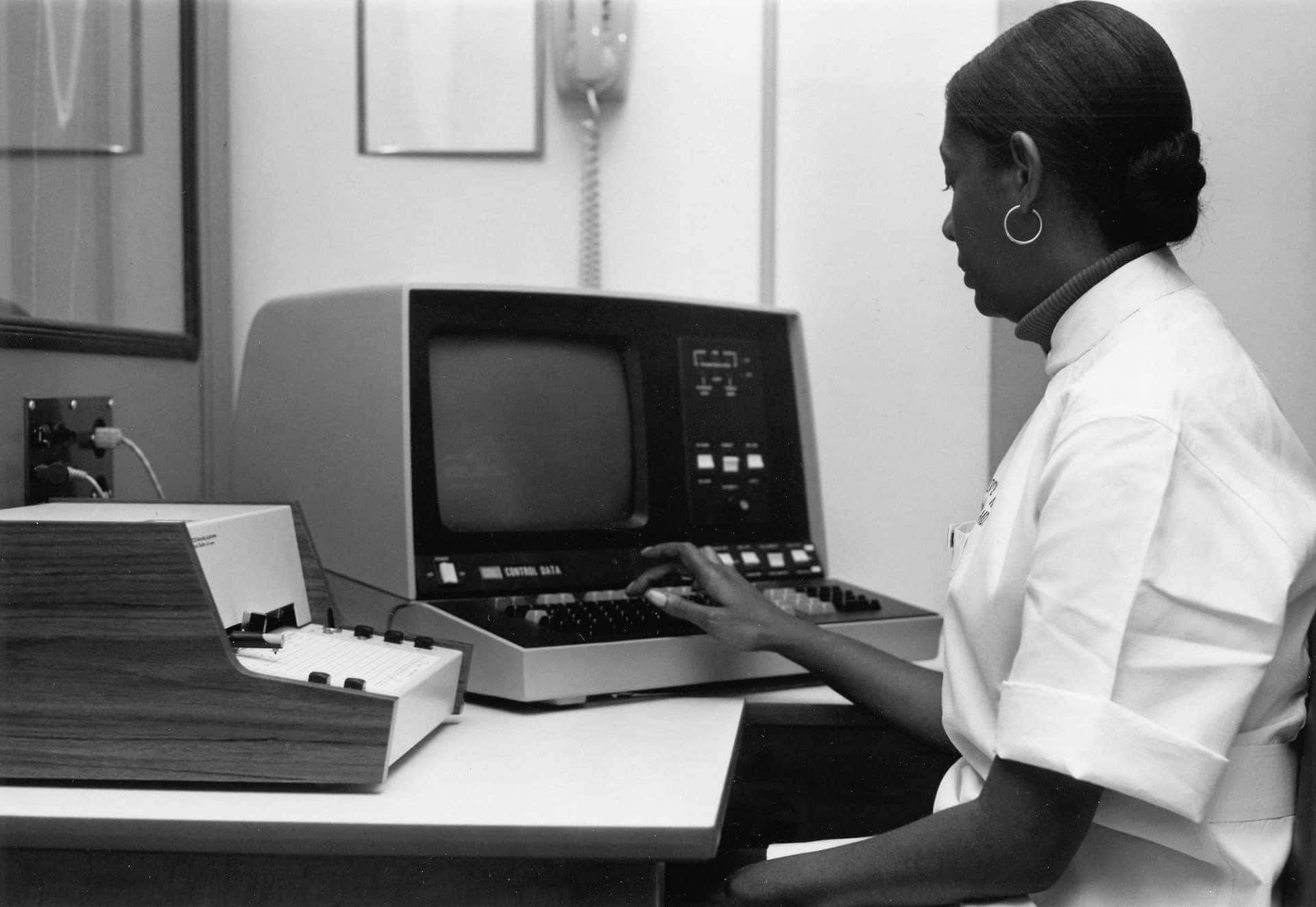 Fotografia de arquivo de uma mulher digitando num computador de monitor de tubo num escritório
