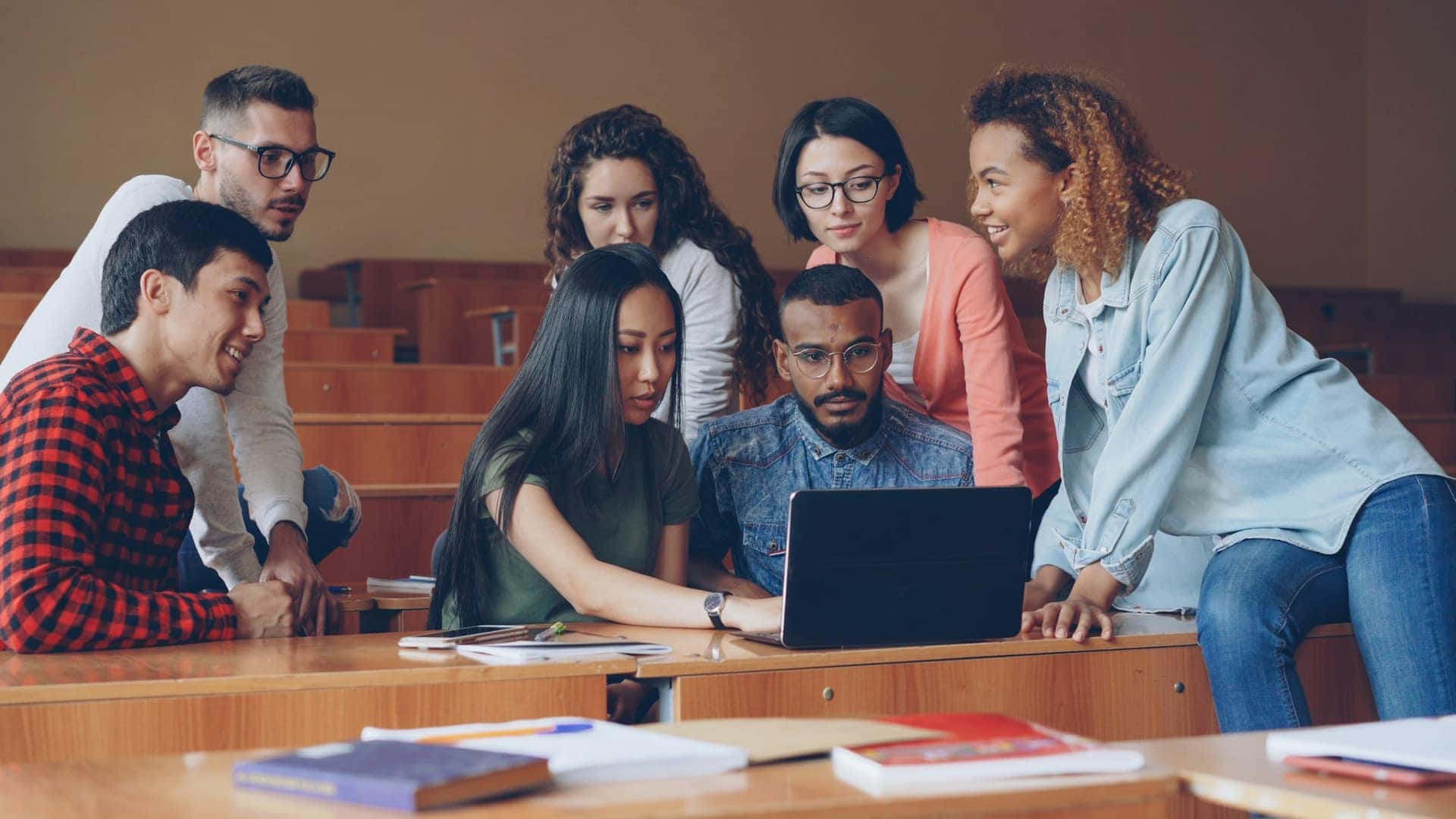 Grupo diverso de estudantes reunido em torno de um notebook numa sala de aula