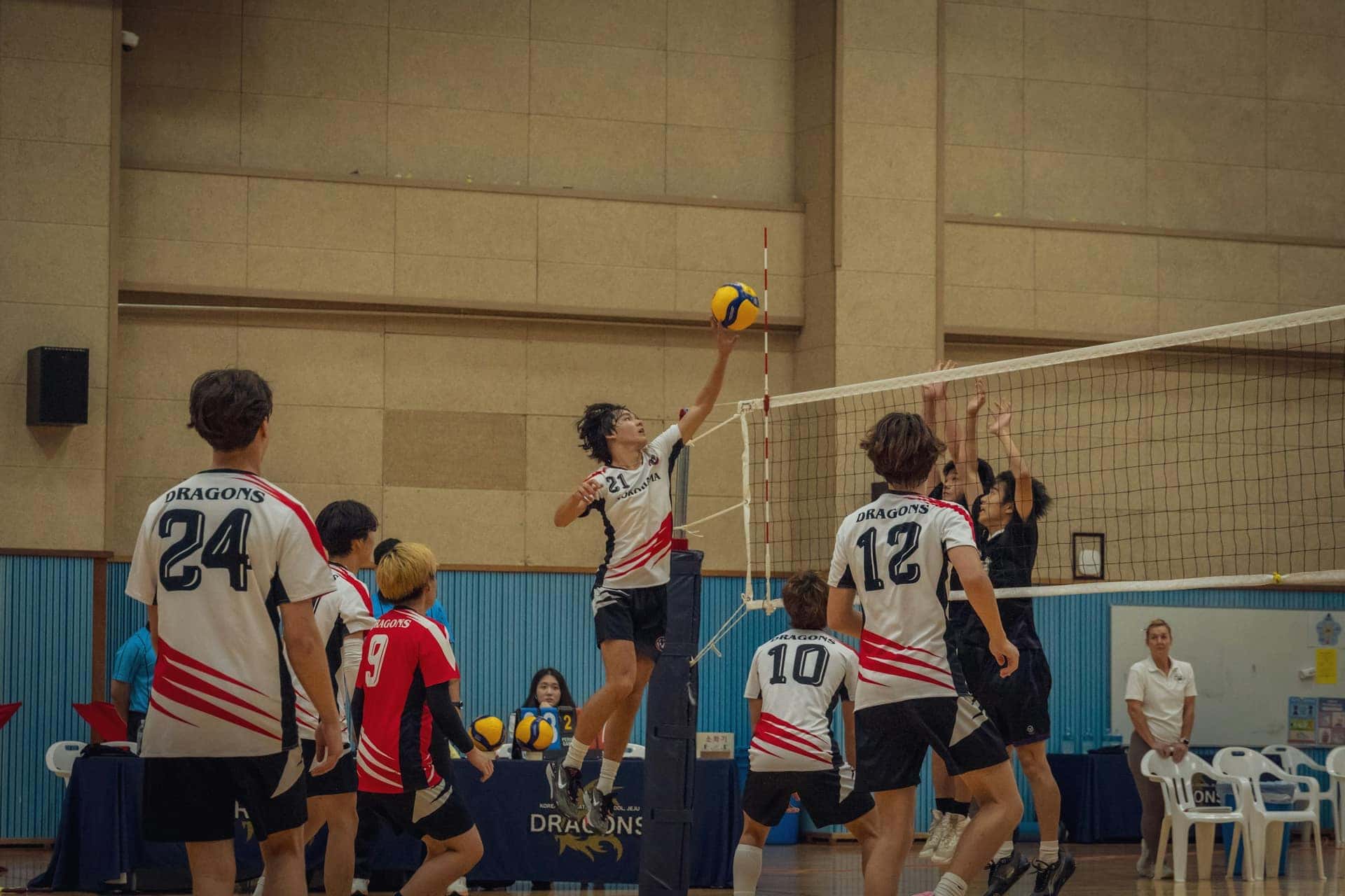 Jovens de uniforme disputam uma partida de vôlei numa quadra coberta