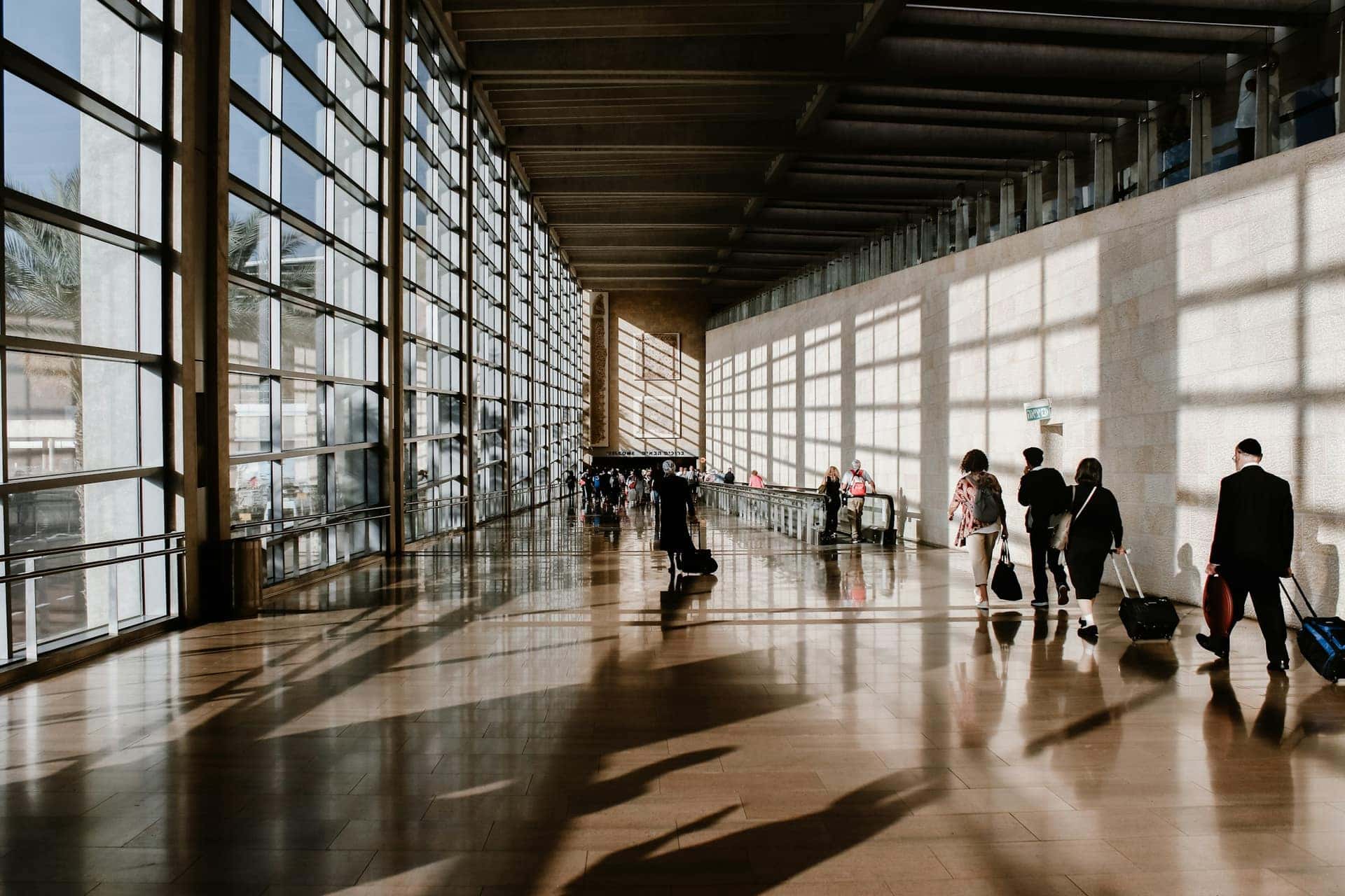 Pessoas caminham com bagagens por um terminal de aeroporto banhado de luz natural
